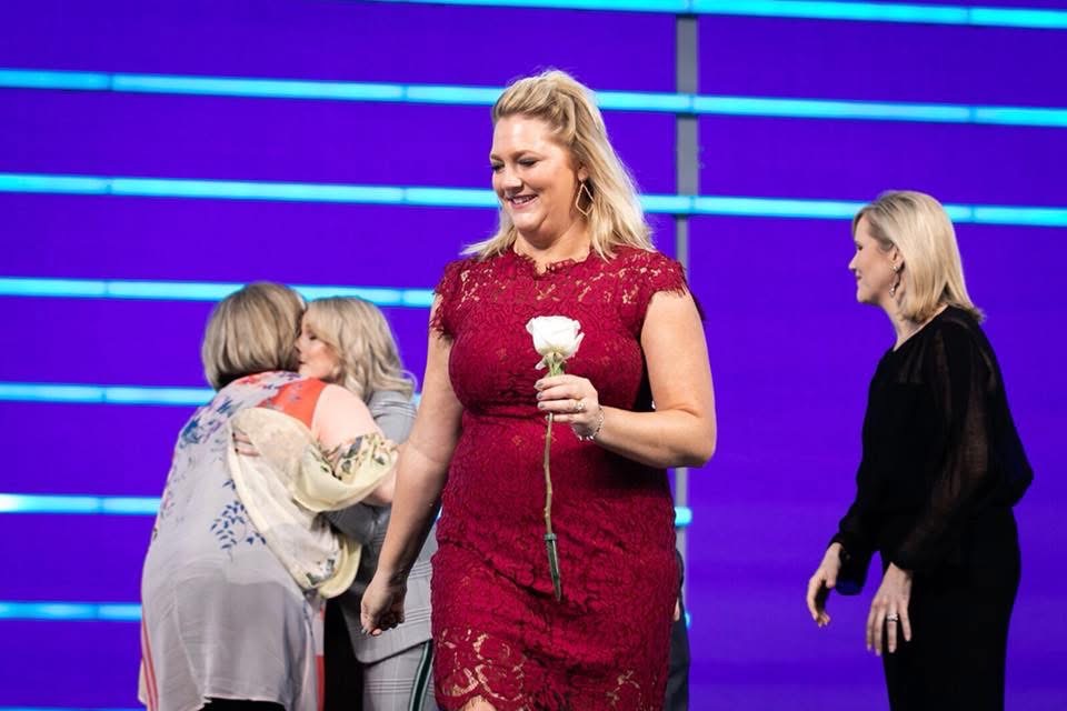 Jen in a red dress holding a rose on stage